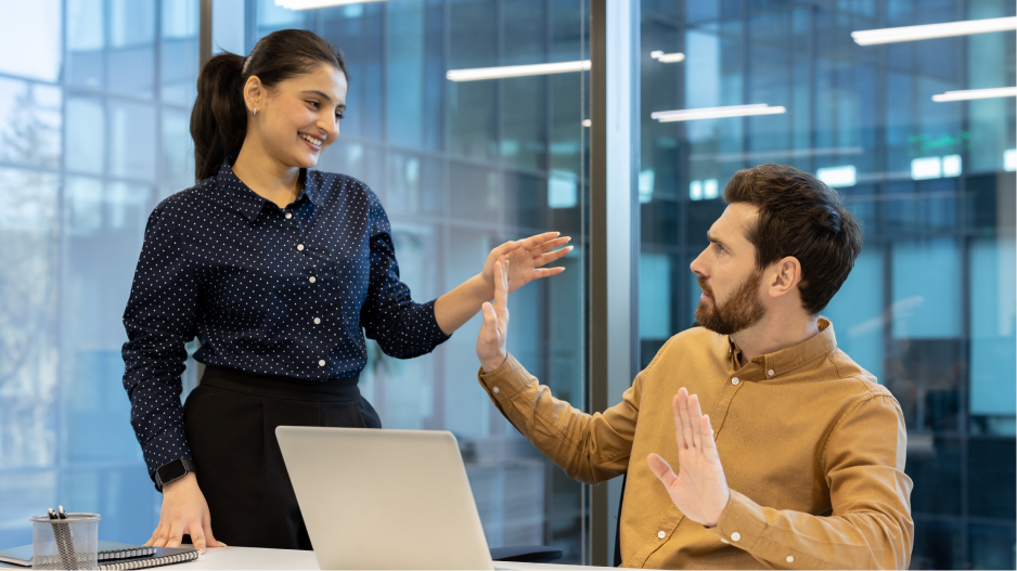/_cms/webroot/Dans un bureau, une personne debout se penche sur une personne assise et l'agrippe, tandis que la personne assise réagit négativement en levant la main.